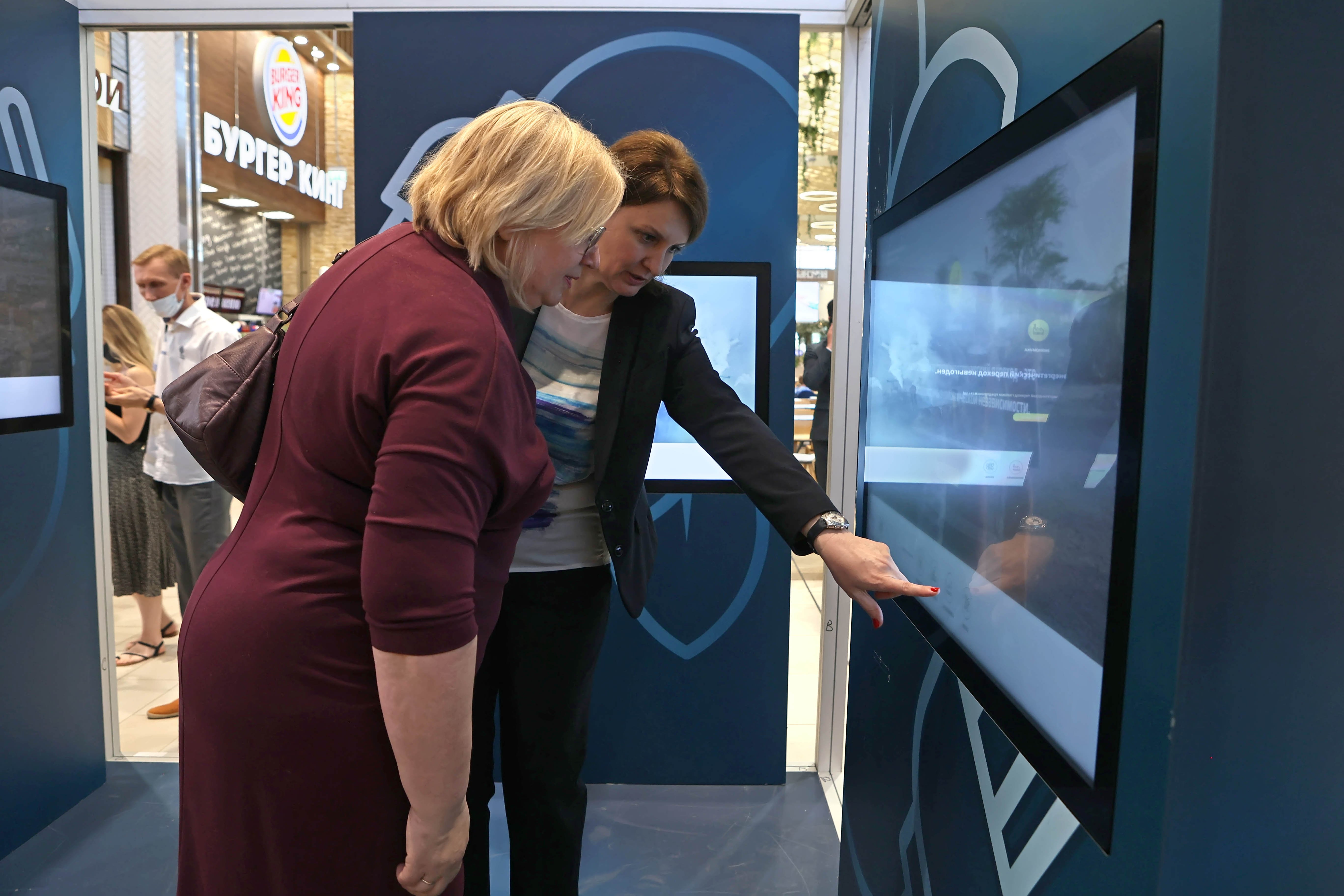 Zwei Frauen stehen an der Station "Erneuerbare Energien" und schauen auf einen Bildschirm. Juni 2021.
